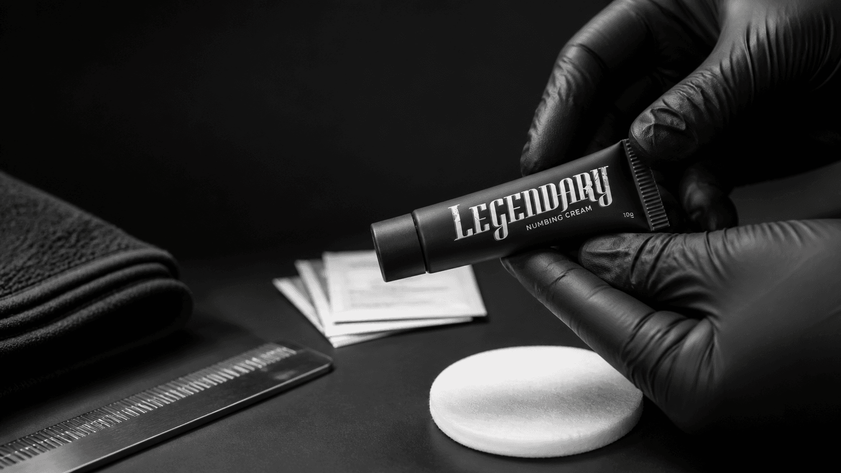 Black-gloved hands holding a Legendary tube on a clean tattoo studio preparation surface